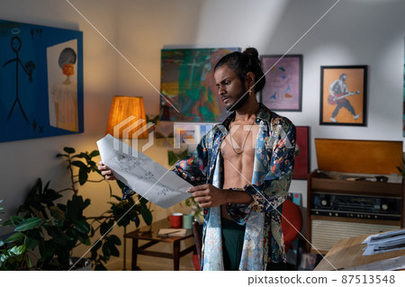 Young inspirated man in non-gendered clothing looking at drawing 87513548