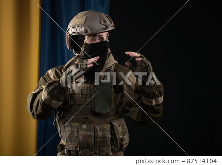 a male soldier in a military uniform and helmet on the background of the national flag of Ukraine 87514104