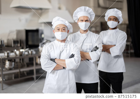 Three well-dressed chefs standing together in the professional kitchen Three well-dressed chefs standing together in the professional kitchen 87515175