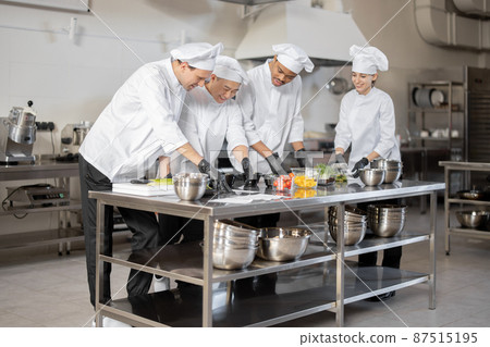 Multiracial team of cooks mixing ingredients for take away food in professional kitchen Multiracial team of cooks mixing ingredients for take away food in professional kitchen 87515195