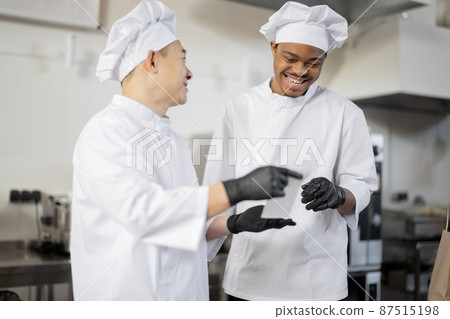 Asian and Latin chefs reading printed order while cooking meals in professional kitchen Asian and Latin chefs reading printed order while cooking meals in professional kitchen 87515198