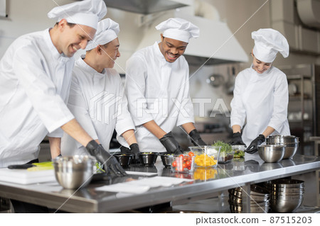 Multiracial team of cooks mixing ingredients for take away food in professional kitchen Multiracial team of cooks mixing ingredients for take away food in professional kitchen 87515203