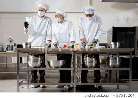 Chefs in face masks prepare takeaway food in professional kitchen Chefs in face masks prepare takeaway food in professional kitchen 87515204
