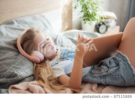 Cute Little girl lying on bed and using tablet at home 87515889