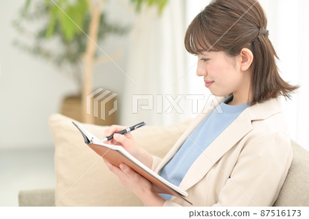 A woman sitting on the sofa and filling out a notebook A woman sitting on the sofa and filling out a notebook 87516173