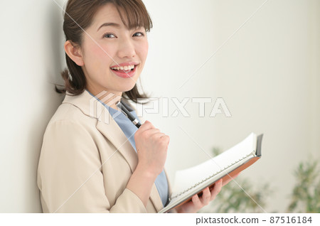 A woman leaning against a wall and filling out a notebook 87516184