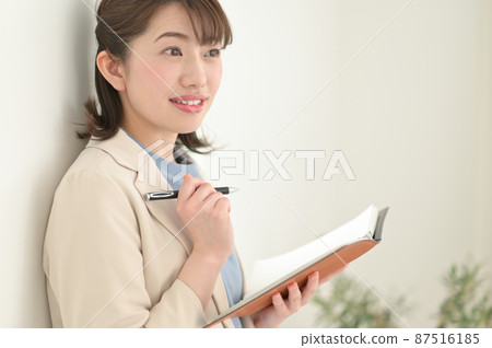 A woman leaning against a wall and filling out a notebook 87516185