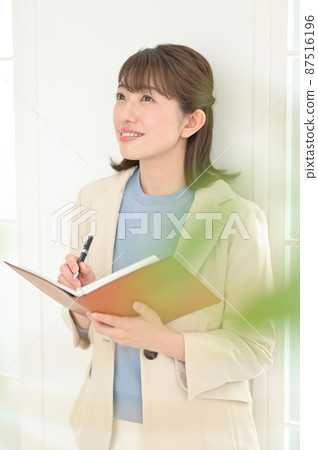A woman leaning against a wall and filling out a notebook A woman leaning against a wall and filling out a notebook 87516196