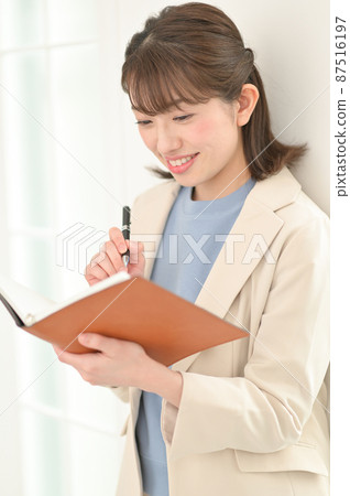 A woman leaning against a wall and filling out a notebook A woman leaning against a wall and filling out a notebook 87516197