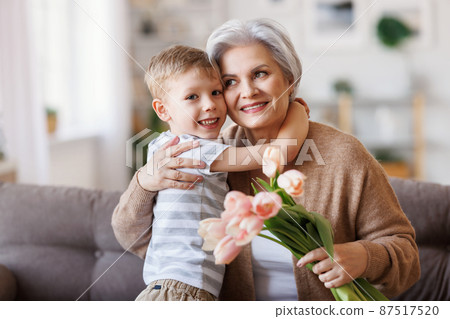 Cheerful little boy giving flowers to grandmother 87517520