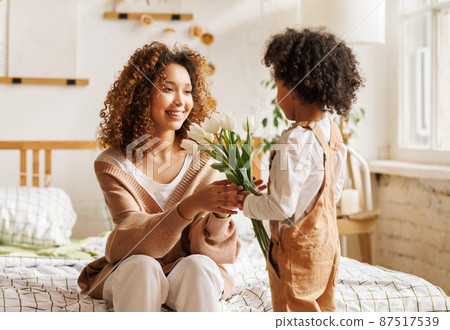Grateful ethnic mother with bouquet hugging son 87517539