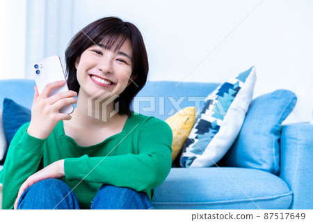 一位年輕女子在明亮的客廳裡使用智能手機 87517649