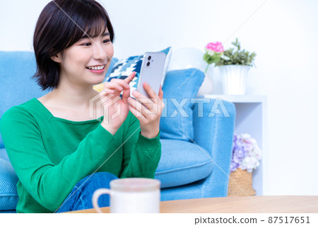 一位年輕女子在明亮的客廳裡使用智能手機 一位年輕女子在明亮的客廳裡使用智能手機 87517651