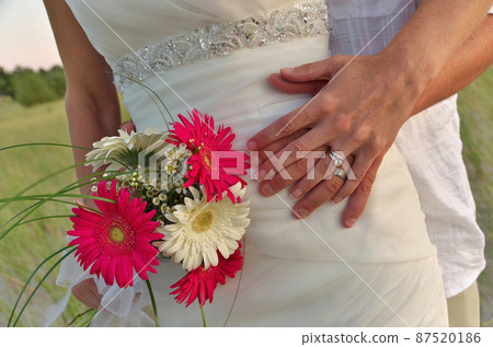 Close up of Groom Putting His Arms Around Bride's Waist Showing Wedding Rings, Dress, and Bouquet Close up of Groom Putting His Arms Around Bride's Waist Showing Wedding Rings, Dress, and Bouquet 87520186