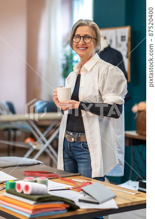 Woman with cup standing at workplace looking at camera 87520400