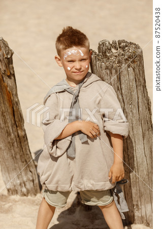 Boy in cozy beige clothes applying sunscreen protection creme on his face. Sun protection  during summer sea vacation. Children healthcare at travel time 87520438