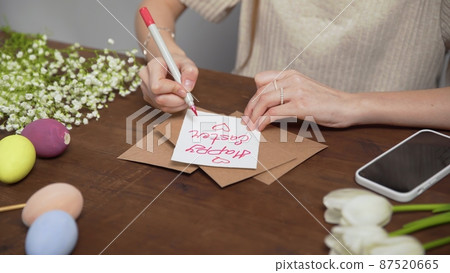 Close-up on a table with items to create a composition for Easter. A woman's hand writes with a red marker: Happy Easter. Christ is risen. Church holiday-Easter Close-up on a table with items to create a composition for Easter. A woman's hand writes with a red marker: Happy Easter. Christ is risen. Church holiday-Easter 87520665