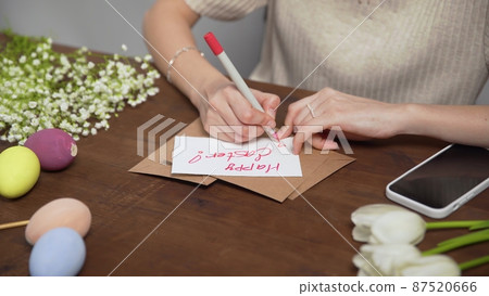 Close-up on a table with items to create a composition for Easter. A woman's hand writes with a red marker: Happy Easter. Christ is risen. Church holiday-Easter Close-up on a table with items to create a composition for Easter. A woman's hand writes with a red marker: Happy Easter. Christ is risen. Church holiday-Easter 87520666