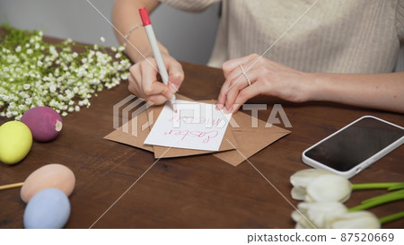 Close-up on a table with items to create a composition for Easter. A woman's hand writes with a red marker: Easter menu. Christ is risen. Church holiday-Easter Close-up on a table with items to create a composition for Easter. A woman's hand writes with a red marker: Easter menu. Christ is risen. Church holiday-Easter 87520669