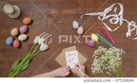 Top view of a table with items to create a composition for Easter. A woman's hand writes with a red marker: April 24. Christ is risen. Church holiday-Easter Top view of a table with items to create a composition for Easter. A woman's hand writes with a red marker: April 24. Christ is risen. Church holiday-Easter 87520694