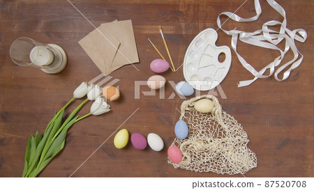 Top view of a table with items to create a composition for Easter. Women's hands put Easter eggs on the table. Church holiday-Easter Top view of a table with items to create a composition for Easter. Women's hands put Easter eggs on the table. Church holiday-Easter 87520708