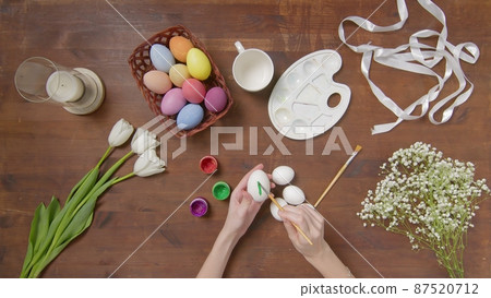 Top view of a table with items to create a composition for Easter. Women's hands paint Easter eggs with colored paint. Church holiday-Easter Top view of a table with items to create a composition for Easter. Women's hands paint Easter eggs with colored paint. Church holiday-Easter 87520712