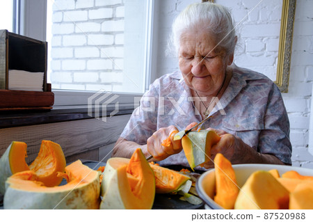 Old woman cuts and pills yellow pumpkin, cooking pumpkin soup, retirement life, selective focus Old woman cuts and pills yellow pumpkin, cooking pumpkin soup, retirement life, selective focus 87520988