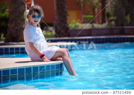 Portrait of happy child girl in white dress relaxing on swimming pool side on sunny summer day during tropical holidays 87521489