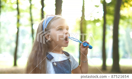 Little happy child girl blowing soap bubbles outdoors in summer park. Little happy child girl blowing soap bubbles outdoors in summer park. 87521654