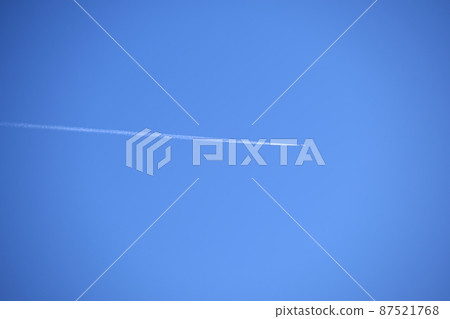 Distant passenger jet plane flying on high altitude on clear blue sky leaving white smoke trace of contrail behind. Air transportation concept. 87521768