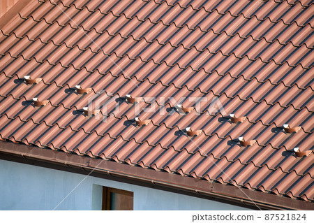 Closeup snow guard for safety in winter on house roof top covered with steel shingles. Tiled covering of building Closeup snow guard for safety in winter on house roof top covered with steel shingles. Tiled covering of building 87521824