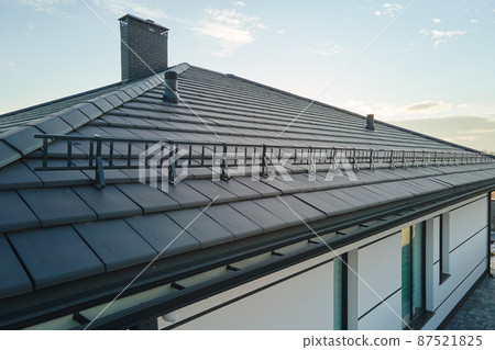 Closeup snow guard for safety in winter on house roof top covered with ceramic shingles. Tiled covering of building Closeup snow guard for safety in winter on house roof top covered with ceramic shingles. Tiled covering of building 87521825