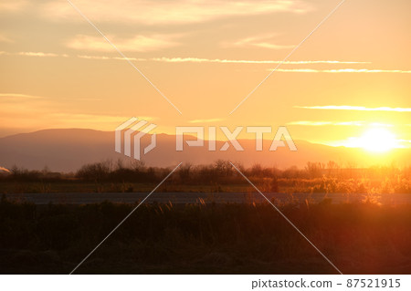 Beautiful evening panoramic landscape with bright setting sun over distant mountain peaks and asphalt road in front at sunset Beautiful evening panoramic landscape with bright setting sun over distant mountain peaks and asphalt road in front at sunset 87521915