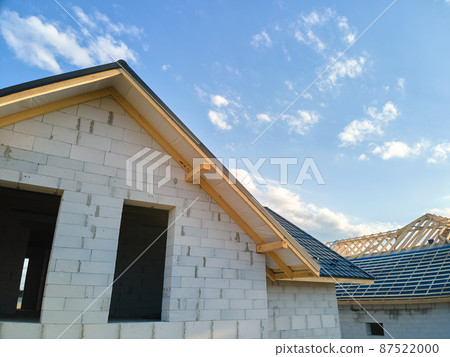 Aerial view of unfinished house with aerated lightweight concrete walls and wooden roof frame covered with metallic tiles under construction. 87522000