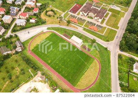 Aerial view of sports stadium with red running tracks and green grass football field near school building in rural area. Aerial view of sports stadium with red running tracks and green grass football field near school building in rural area. 87522004