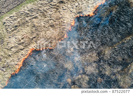 Aerial view of grassland field burning with red fire during dry season. Natural disaster and climate change concept Aerial view of grassland field burning with red fire during dry season. Natural disaster and climate change concept 87522077