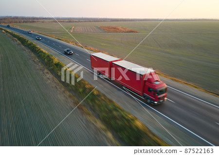 Aerial view of blurred fast moving semi-truck with cargo trailer driving on highway hauling goods in evening. Delivery transportation and logistics concept Aerial view of blurred fast moving semi-truck with cargo trailer driving on highway hauling goods in evening. Delivery transportation and logistics concept 87522163