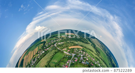 Aerial view from high altitude of little planet earth with small village houses and distant green cultivated agricultural fields with growing crops on bright summer day 87522289