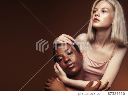 two pretty girls african and caucasian blond posing cheerful together on brown background, ethnicity diverse lifestyle people concept two pretty girls african and caucasian blond posing cheerful together on brown background, ethnicity diverse lifestyle people concept 87523630