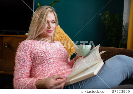 A girl reads a book with a cup in her hand while resting. A girl reads a book with a cup in her hand while resting. 87523909