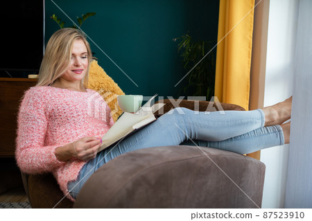 A girl reads a book with a cup in her hand while resting. A girl reads a book with a cup in her hand while resting. 87523910