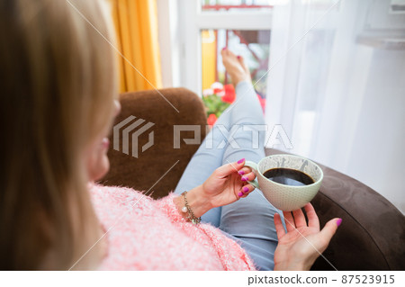A young woman holds a cup and looks ahead. 87523915
