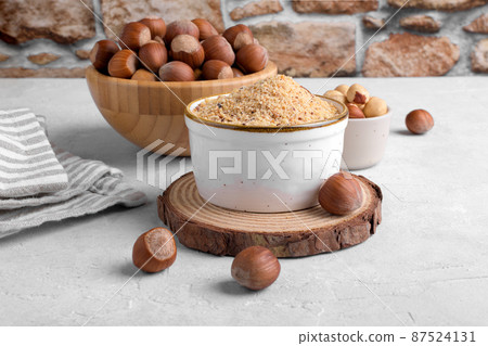 Raw Organic Ground Hazelnut Flour in a Bowl with whole nuts on grey stone background. Alternative nut flour 87524131