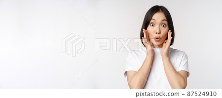 Close up portrait of asian girl looking surprised, wow face, reacting amazed at smth, standing in white tshirt over studio background, isolated Close up portrait of asian girl looking surprised, wow face, reacting amazed at smth, standing in white tshirt over studio background, isolated 87524910