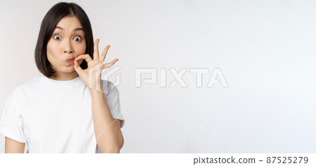 Image of young asian woman showing silence gesture, zipping mouth, seal lips, make promise, standing over white background 87525279