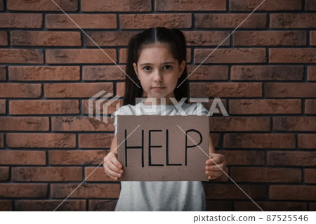 Sad little girl with sign HELP near brick wall. Child in danger Sad little girl with sign HELP near brick wall. Child in danger 87525546