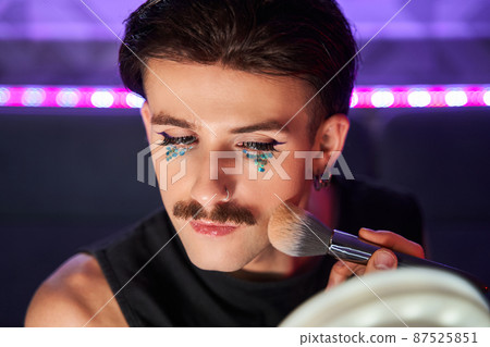 Feminine man applying blushes at his chicks with concentrated face 87525851