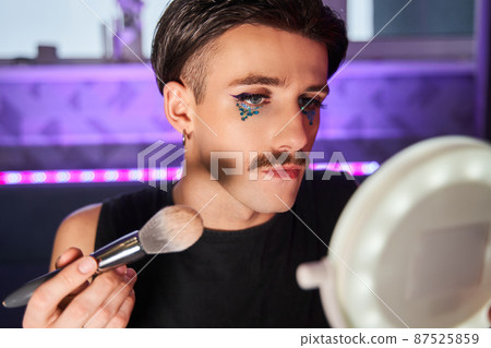 Caucasian male person applying blushes at his chicks while looking at the camera Caucasian male person applying blushes at his chicks while looking at the camera 87525859