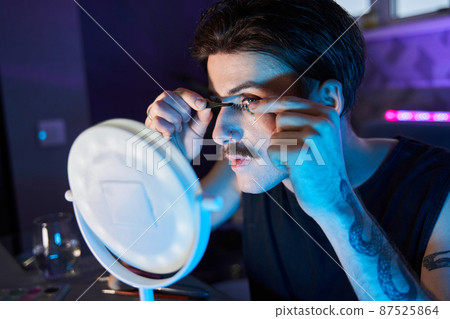 Man applying lushes with special brush and feeling attentive while doing make-up Man applying lushes with special brush and feeling attentive while doing make-up 87525864