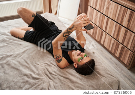 Guy with tattoos laying at the bed and shooting himself at the smartphone 87526006